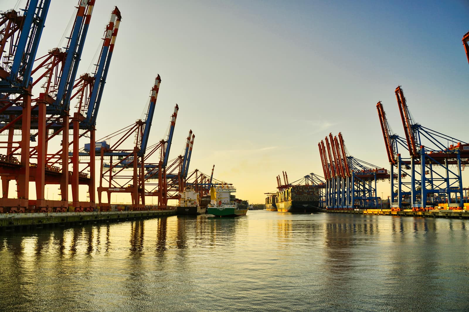 A commercial cargo port at golden hour with cranes and vessels